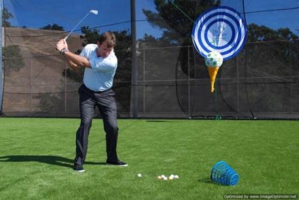 Man driving golf ball from tee on artificial turf