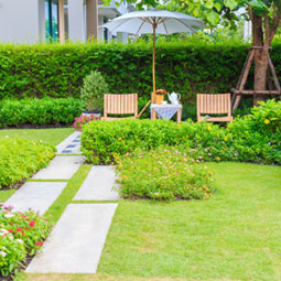 a wooden table set and umbrella in a beautiful garden and other ideas for property managers who want to save money on landscaping using artificial grass
