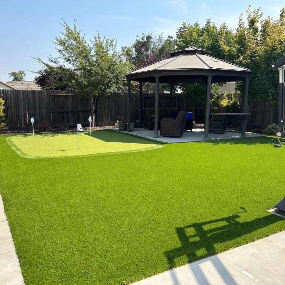 Backyard putting green installation featuring vibrant artificial turf, surrounded by a gazebo and landscaped greenery, showcasing a low-maintenance outdoor space ideal for residential enjoyment.
