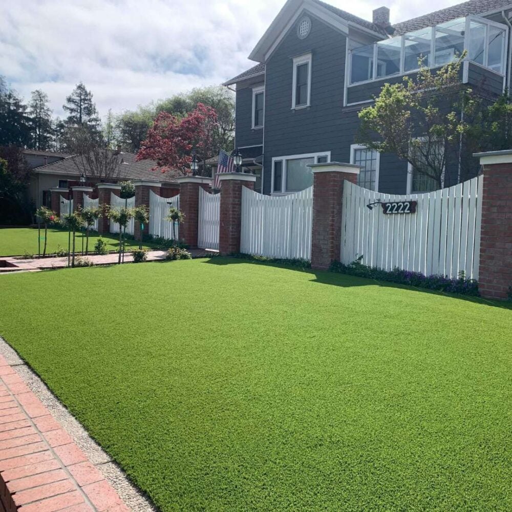 Front yard featuring lush, vibrant artificial turf installation by Heavenly Greens, with a white picket fence and a charming residential house in the background, showcasing a low-maintenance landscape design ideal for Bay Area homes.