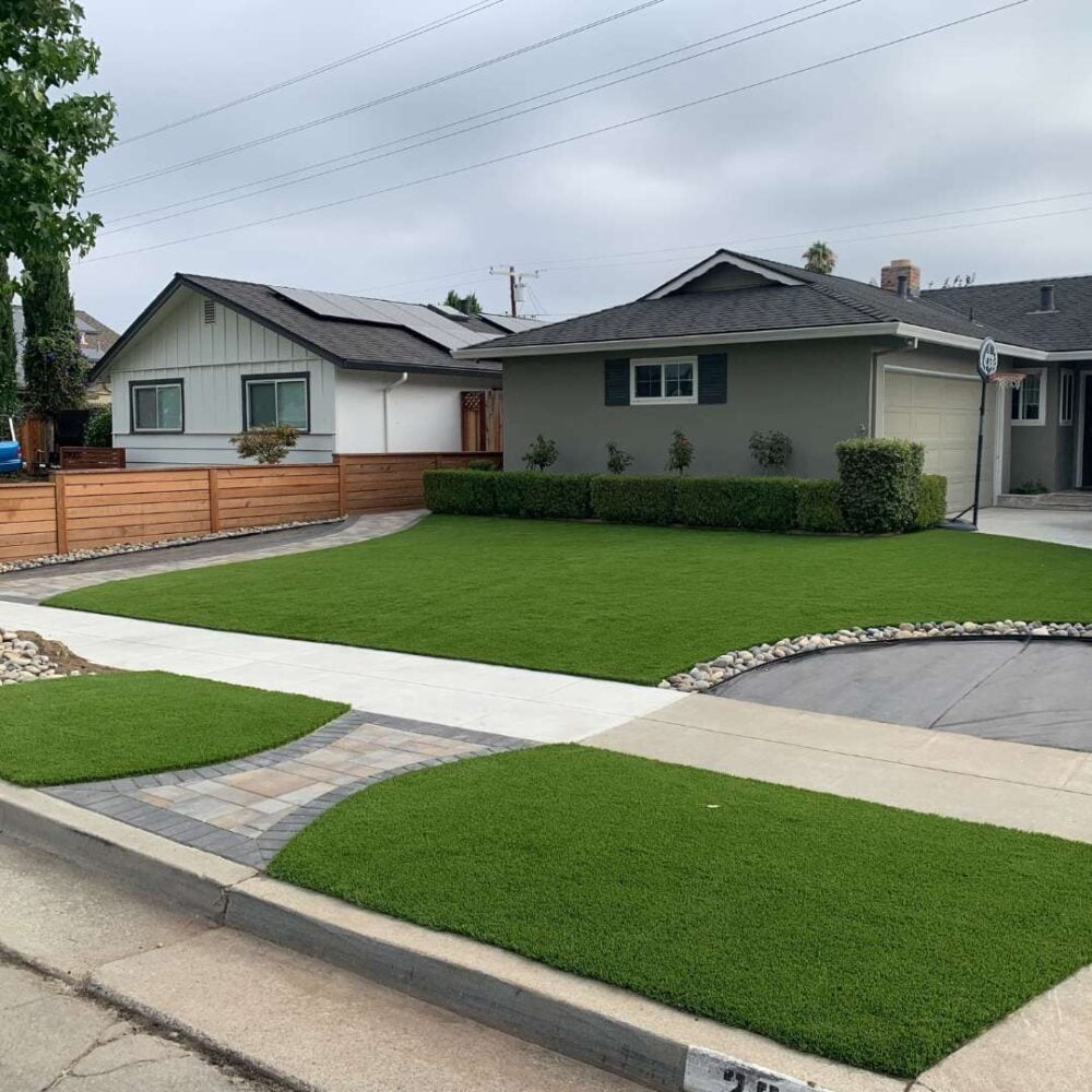 Front yard featuring vibrant artificial turf installation with manicured shrubs, modern homes in the background, and a clean concrete pathway, showcasing Heavenly Greens' landscaping expertise.