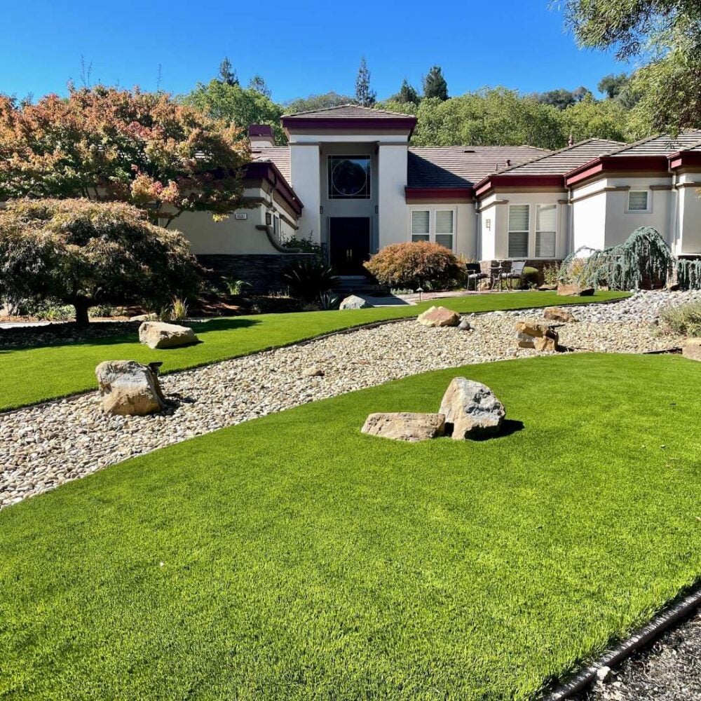 Front yard landscape featuring vibrant artificial turf, decorative stones, and a modern home, showcasing Heavenly Greens' premium installation services for low-maintenance outdoor spaces.