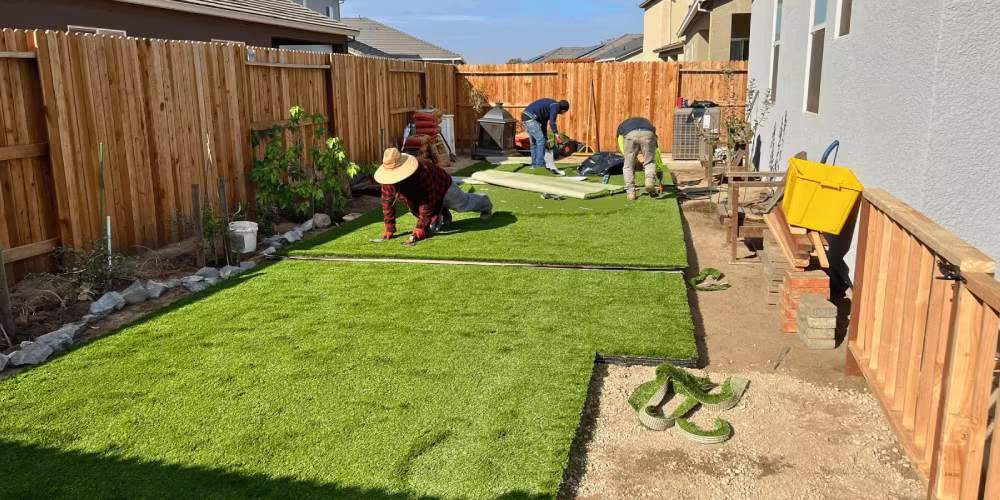 Workers installing artificial grass in a residential backyard, showcasing lush turf and preparation for a low-maintenance lawn.