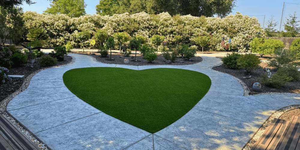 Heart-shaped patch of artificial grass surrounded by landscaped garden and decorative stone pathway, illustrating eco-friendly lawn solution for Bay Area backyards.